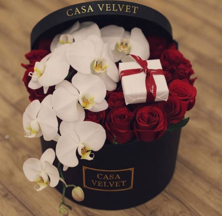 Arreglo floral de rosas rojas y orquídeas blancas en una caja cilíndrica color negro